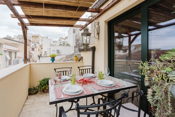 A rooftop terrace with a table set for dining, surrounded by chairs, and overlooking a cityscape.