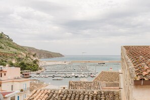 A coastal marina with boats, buildings with tiled roofs, and a hilly landscape.