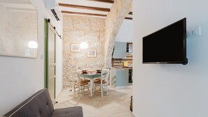 Un espacio habitable compacto con sofá, una mesa de comedor con sillas, zona de cocina y televisor montado.