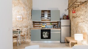 Una cocina compacta con horno integrado, un pequeño comedor con mesa y sillas, y una pared de piedra rústica.