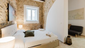 Un dormitorio con pared de piedra, una cama con cabecera, una ventana, un sofá y un mapa en la pared.