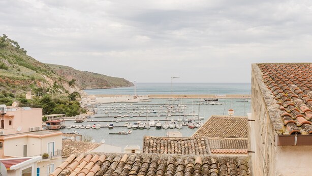 Un puerto costero con barcos, edificios con tejados de baldosas y un paisaje montañoso.
