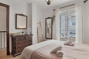 A bedroom with a bed, dresser, mirror, and a view of a balcony.