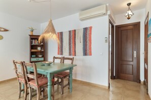 A dining area with a wooden table and chairs, a hanging light fixture, and a wall-mounted air conditioner.