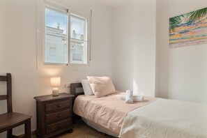 A bedroom with a bed, nightstand, lamp, and a painting of a beach scene.