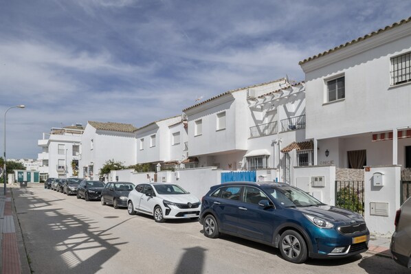 A row of white apartment buildings with parked cars on the street.