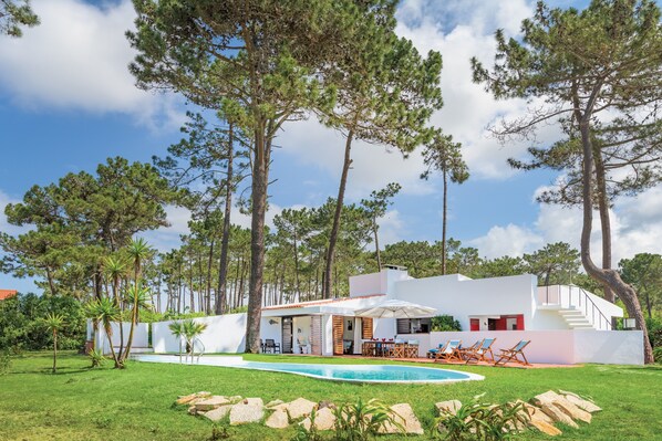 Ein modernes Haus mit Swimmingpool, Sitzgelegenheiten im Freien und hohen Bäumen.