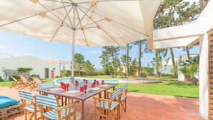 An outdoor patio with a round table, striped chairs, and a large umbrella. - Apartment 'Cerca Do Altinho' with Private Pool, Private Terrace and Wi-Fi (Vila Nova de Milfontes)