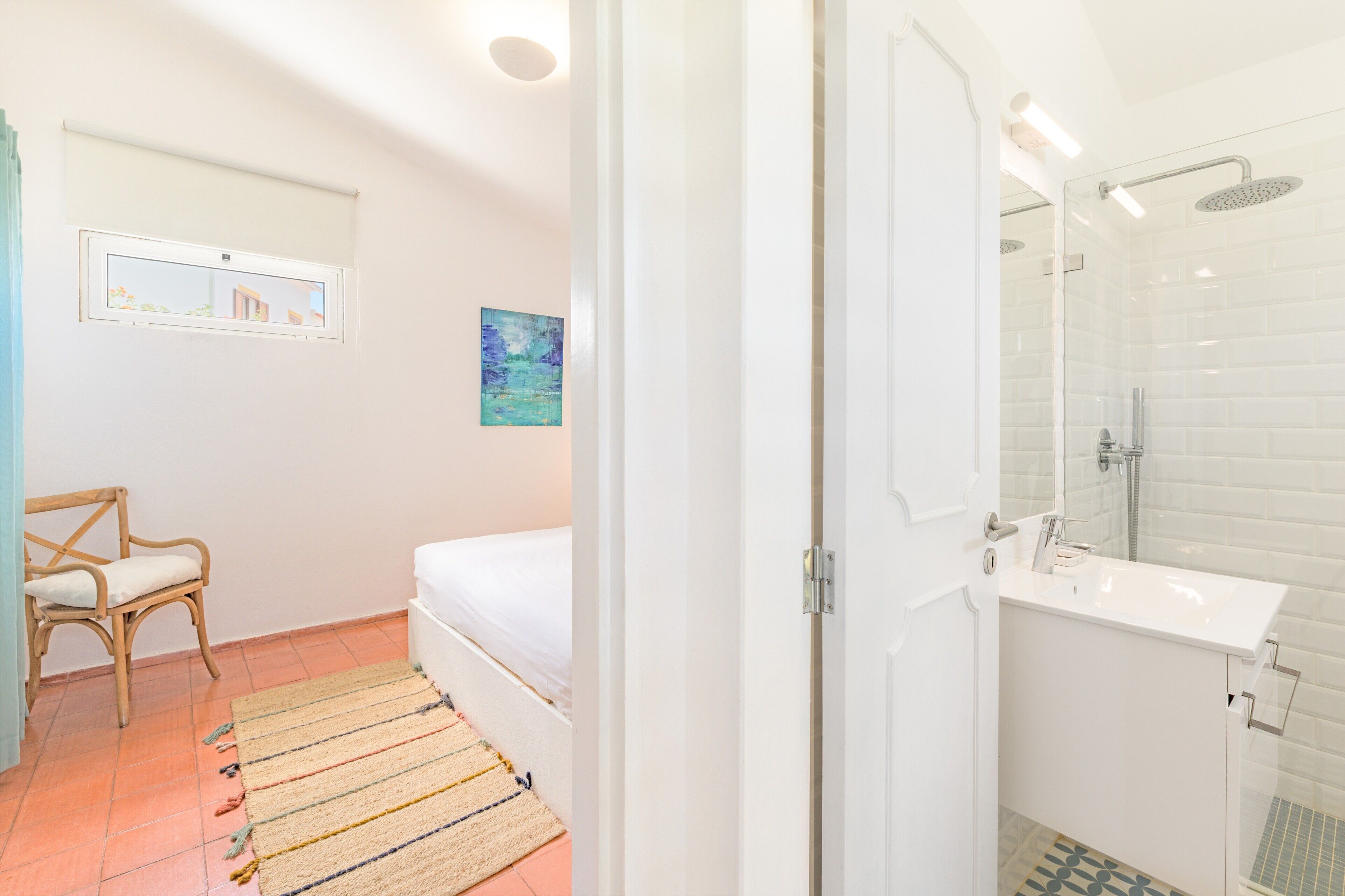 Ein Zimmer mit Bett, Stuhl, Bad mit Dusche und Fenster.