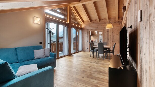 Un intérieur moderne avec un plafond en bois, un canapé bleu, un coin repas et un téléviseur fixé au mur.