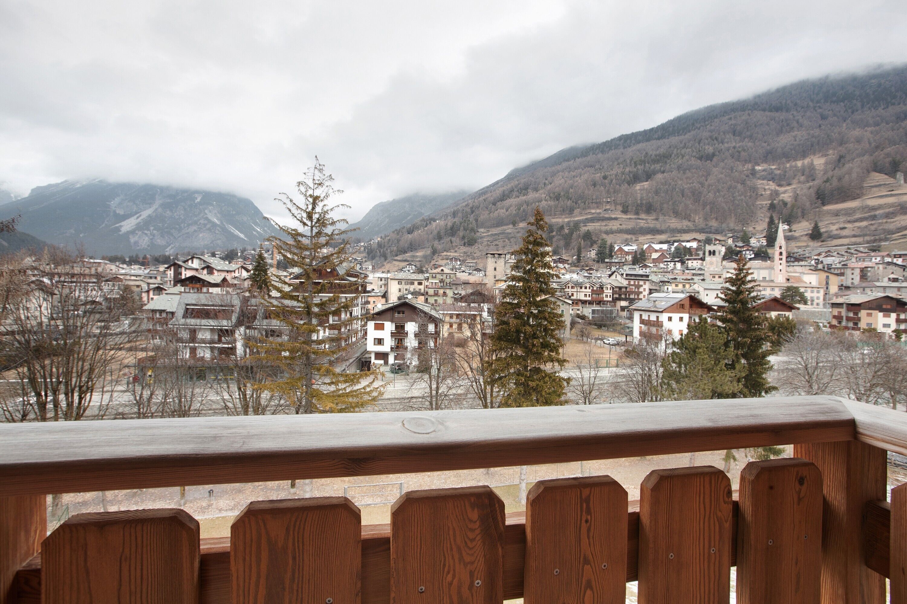 A town with a prominent church tower, surrounded by residential buildings and mountains in the background.