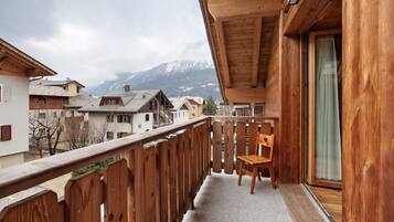 Ein Holzbalkon mit einem Stuhl und Blick auf schneebedeckte Berge sowie benachbarte Gebäude.