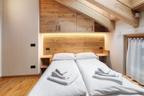 A bedroom with two beds, wooden headboard, built-in nightstands, and a sloped ceiling.