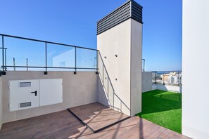 A rooftop with a glass balustrade, a white utility box, a small staircase, and a green artificial turf area.