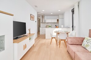 A modern kitchen with white cabinets, a dining area with a table and chairs, and a living area with a sofa.