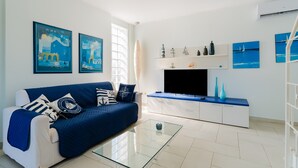 Una sala de estar moderna con un sofá azul, una mesa de centro de cristal, un televisor de pantalla plana y obras de arte con temática náutica.