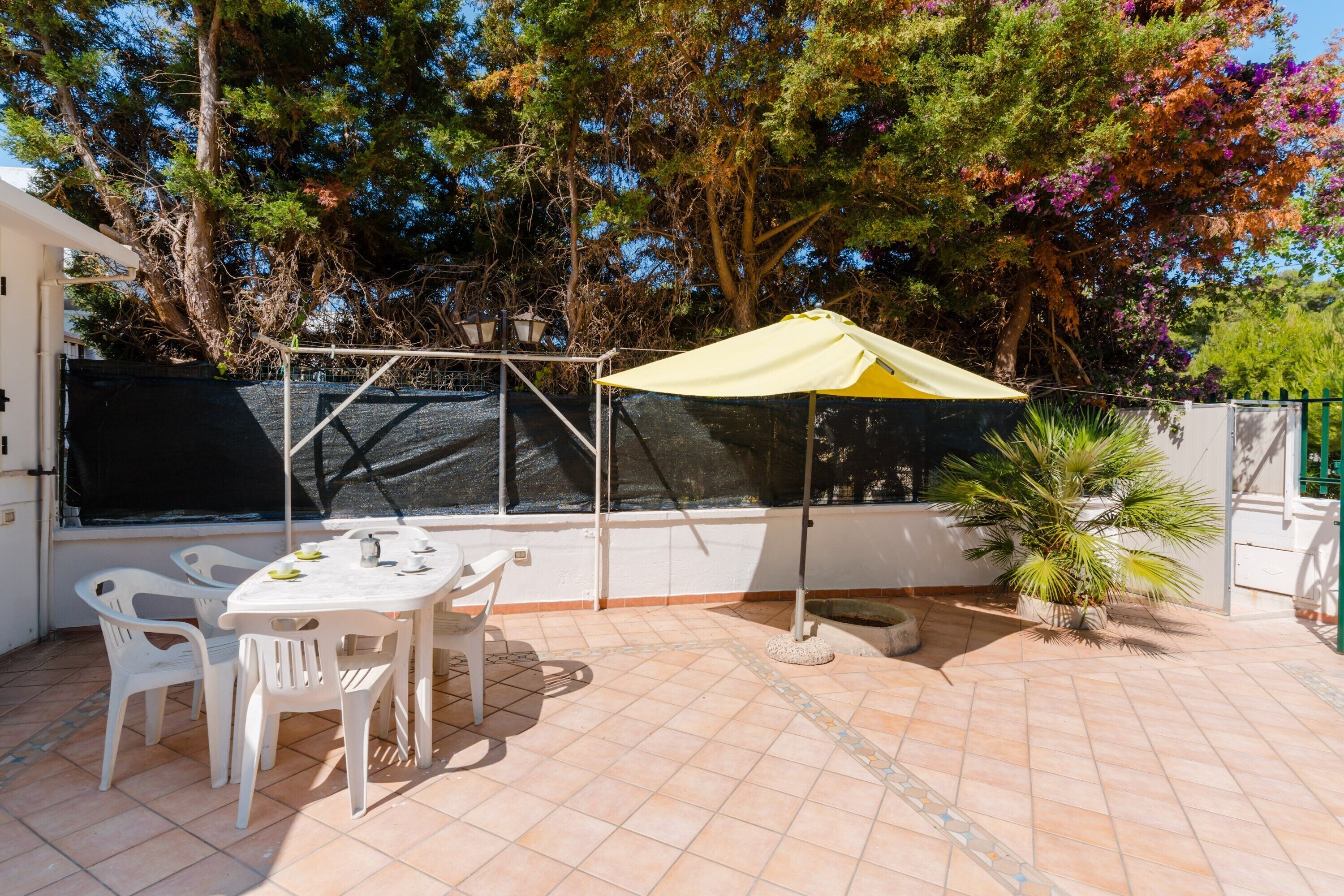 An outdoor patio with a table and chairs, a yellow umbrella, and a potted plant.
