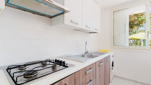 Una cocina con armarios blancos, estufa a gas, pileta y ventana con vista a los árboles.