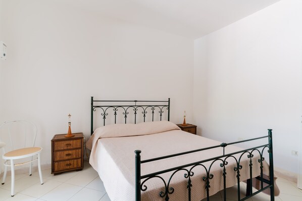 A bedroom with a metal bed frame, a wooden nightstand, a chair, and a bedside table with a lamp. - Holiday Home 'Fontanelle' (Fontanelle)