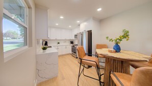 A modern kitchen with white cabinets, a marble countertop, a stainless steel refrigerator, and a dining area with a wooden table and chairs. - Folsom Old Town Escape II - King Bed, A/C, Laundry, Trails, walk to Sutter St (Folsom)