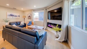 A modern living room with a black leather sofa, a wooden coffee table, and a flat-screen TV mounted on the wall. - Folsom Old Town Escape II - King Bed, A/C, Laundry, Trails, walk to Sutter St (Folsom)