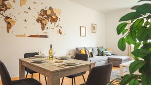 Un coin repas agrémenté d’une carte du monde au mur, une table à manger dressée avec des assiettes et des verres, et un canapé gris en arrière-plan.