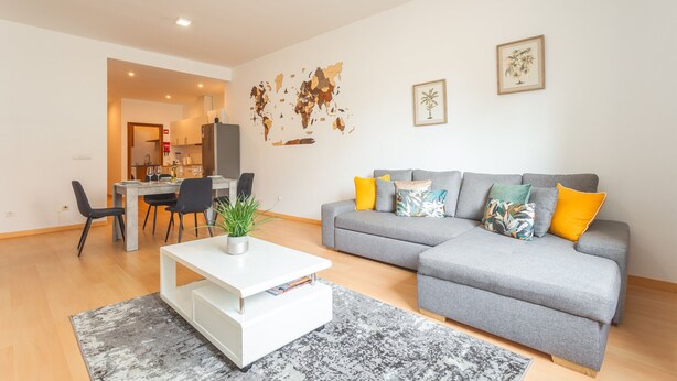 Un salon moderne avec un canapé gris, une table basse et un coin repas comprenant des chaises et une table.
