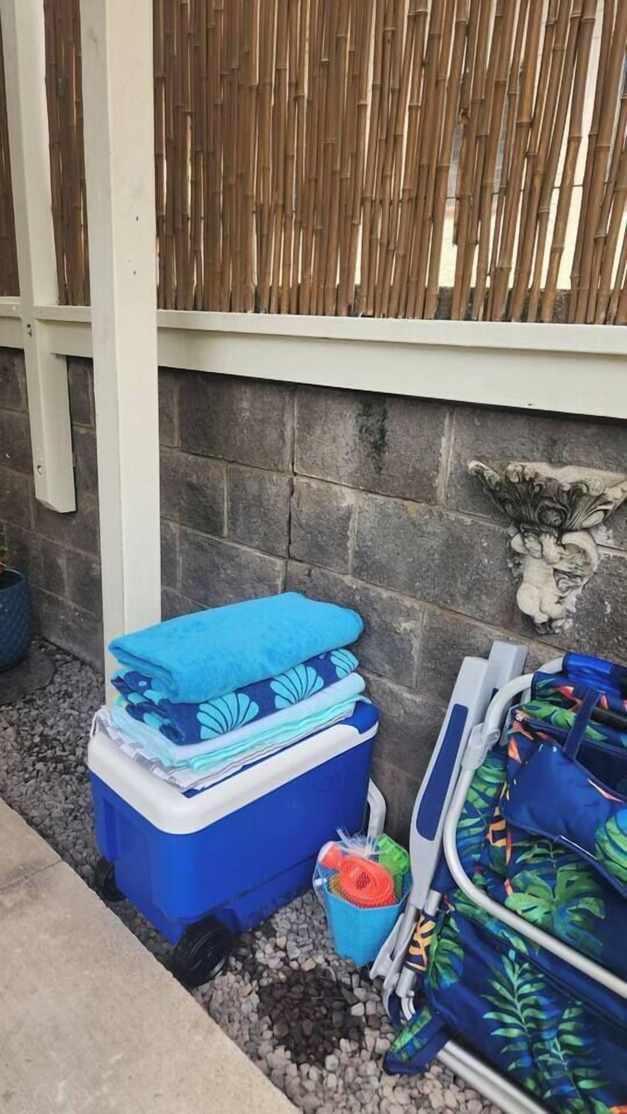 A blue cooler with folded clothes and a small container with a colorful item on a gravel surface.