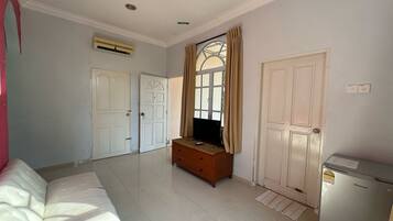 A room with a white sofa, a wooden dresser, a television, and a refrigerator.