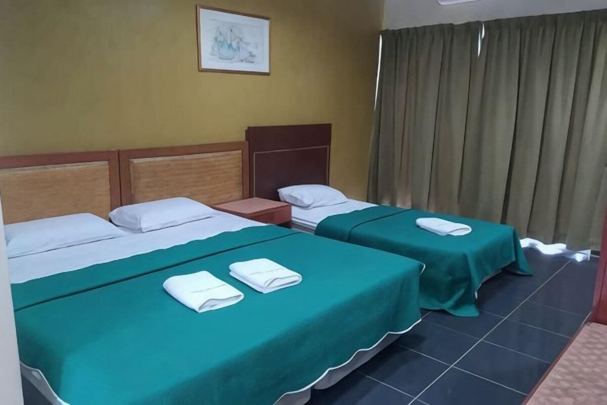 Una habitación con dos camas, cada una con cubrecama verde y almohadas blancas, cabecera de madera, mesita de noche y un cuadro en la pared.