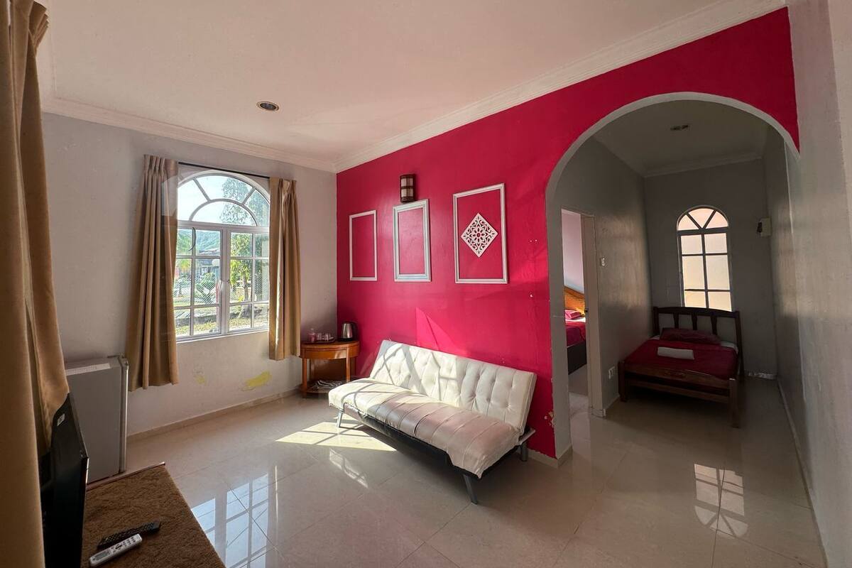 Una stanza con un divano bianco, un letto, una finestra e una parete rossa.
