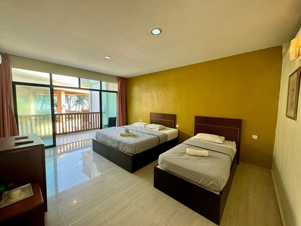 Habitación de hotel con dos camas, un escritorio y un ventanal con vistas a un balcón.