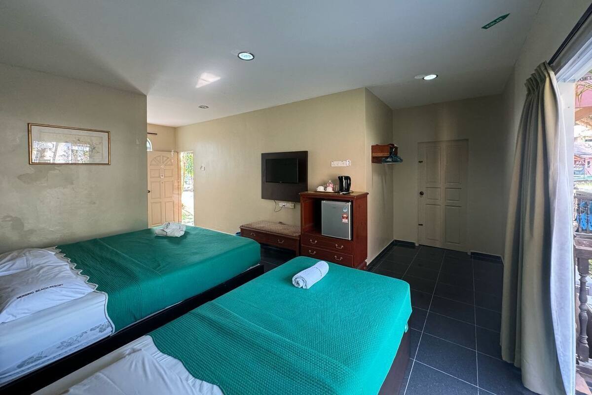 Camera d'albergo con due letti, una TV, un piccolo mobile e una porta che dà su un balcone.