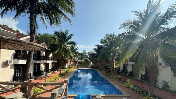 Un área de piscina con un tobogán acuático, rodeada de palmeras y edificios con balcones.