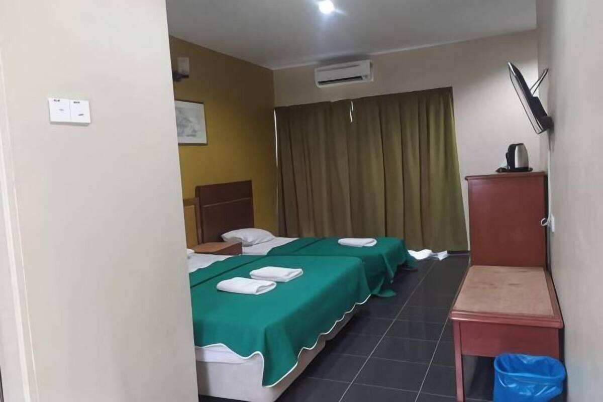 Una camera d'albergo con due letti, una scrivania, una sedia, un cestino, una televisione e una tenda.