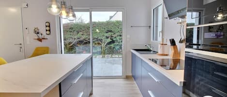A modern kitchen with a large island, grey cabinetry, and a view to the outdoors.
