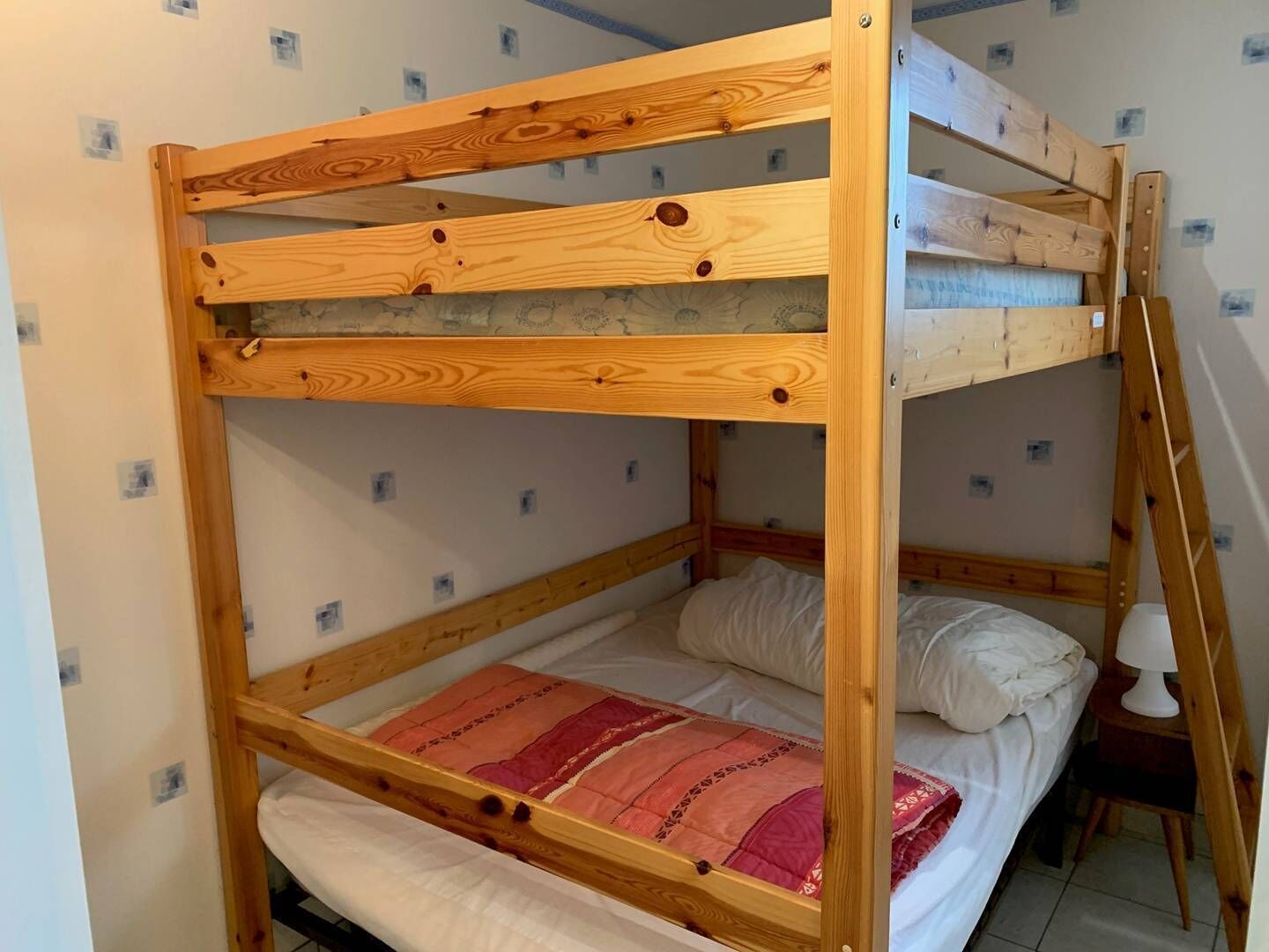 Un lit superposé avec une structure en bois, une literie blanche et une couverture rouge et rose.