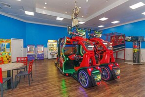 Una habitación con juegos de arcade, una zona de juegos temática de coches rojos y una mesa con sillas.