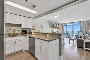 A modern kitchen with granite countertops, white cabinetry, and a view to a balcony.