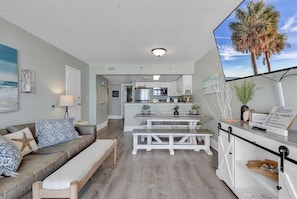 A modern living room with a sofa, a dining table, and a kitchen in the background.