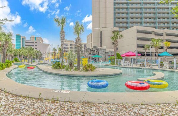 A pool area with multiple inflatable rings, palm trees, and a hotel building in the background.