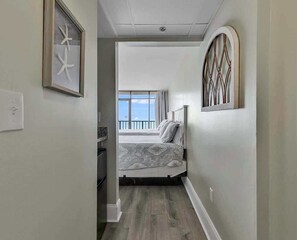 A narrow hallway leading to a bedroom with a bed, a window, and a balcony. - Sand Dunes 1147 & 1148 (Myrtle Beach)