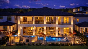 Una casa grande de dos pisos con piscina, varios balcones e iluminación exterior.