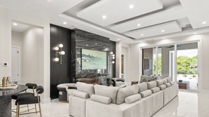 Una sala de estar moderna con un amplio sofá modular, un comedor con mesa redonda y una cocina al fondo.