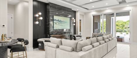 A modern living room with a large sectional sofa, a dining area with a round table, and a kitchen in the background.