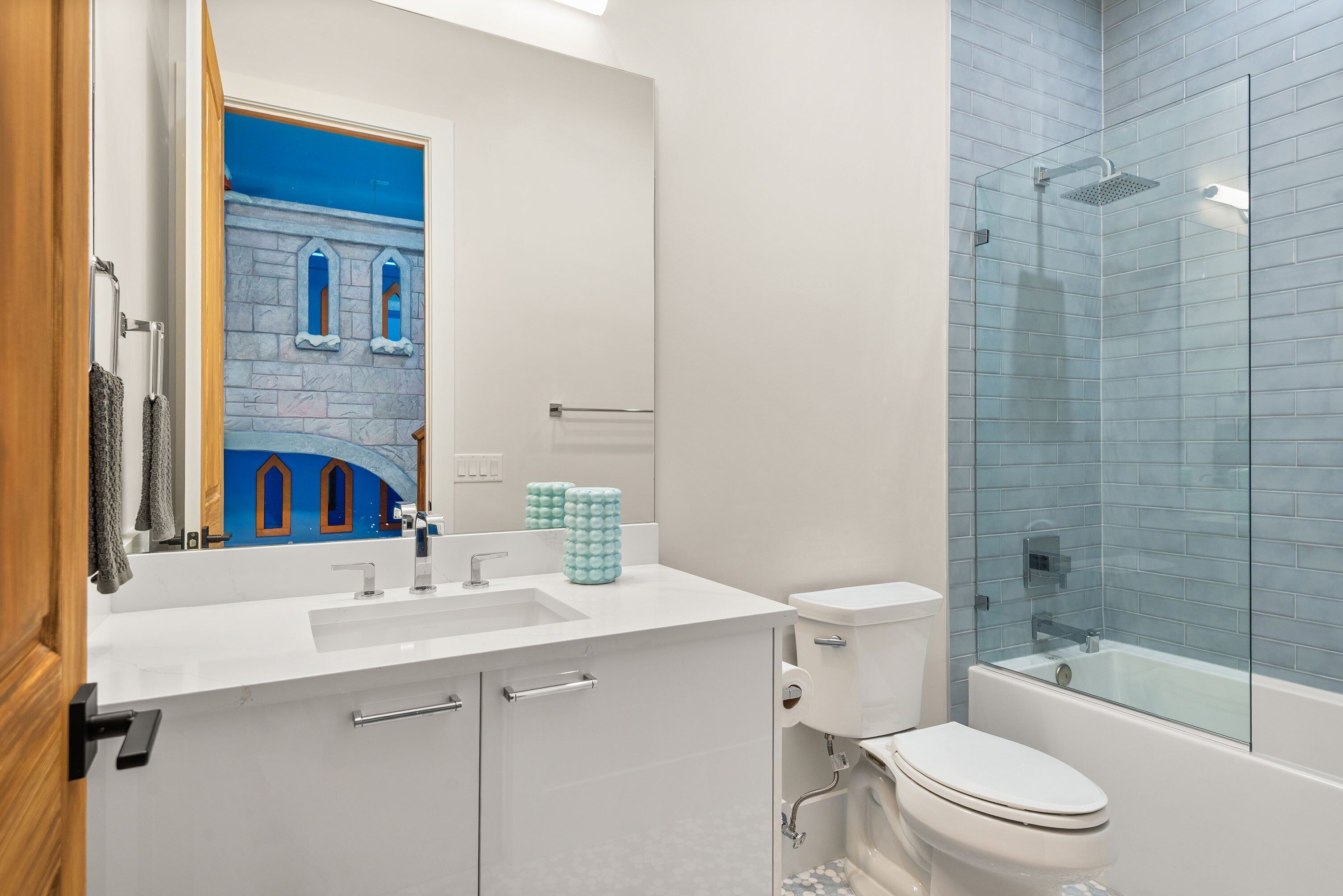 A modern bathroom with a large mirror, a sink, a toilet, and a glass-enclosed shower.