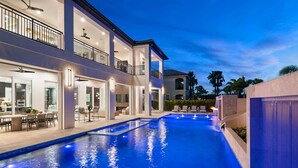 Una casa moderna de dos pisos con piscina, mobiliario exterior e iluminado balcón.