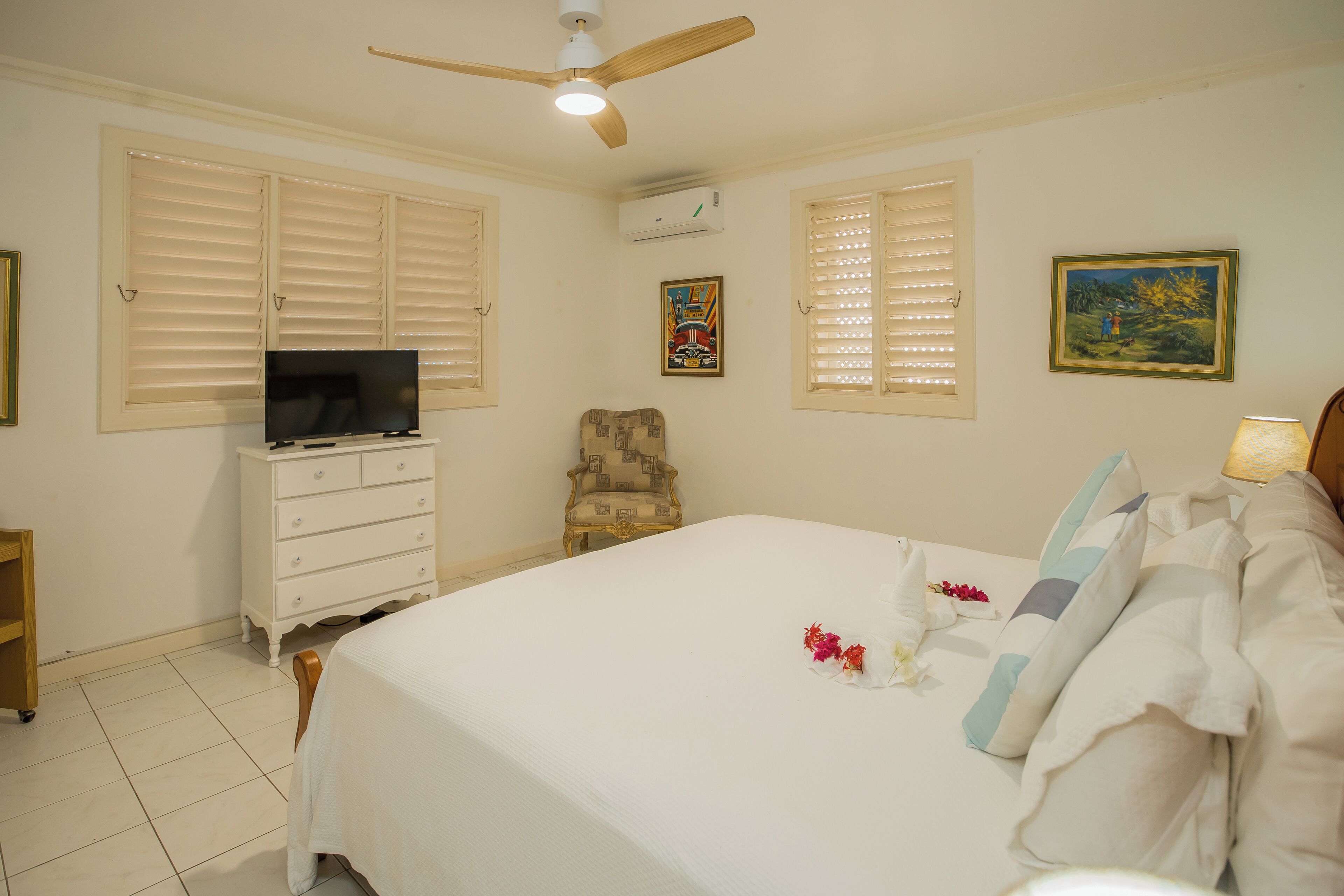 Une chambre à coucher avec un lit, un téléviseur posé sur une commode, une chaise et un tableau accroché au mur.