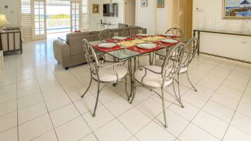 A dining area with a glass table set for six, surrounded by metal chairs with cushioned seats.