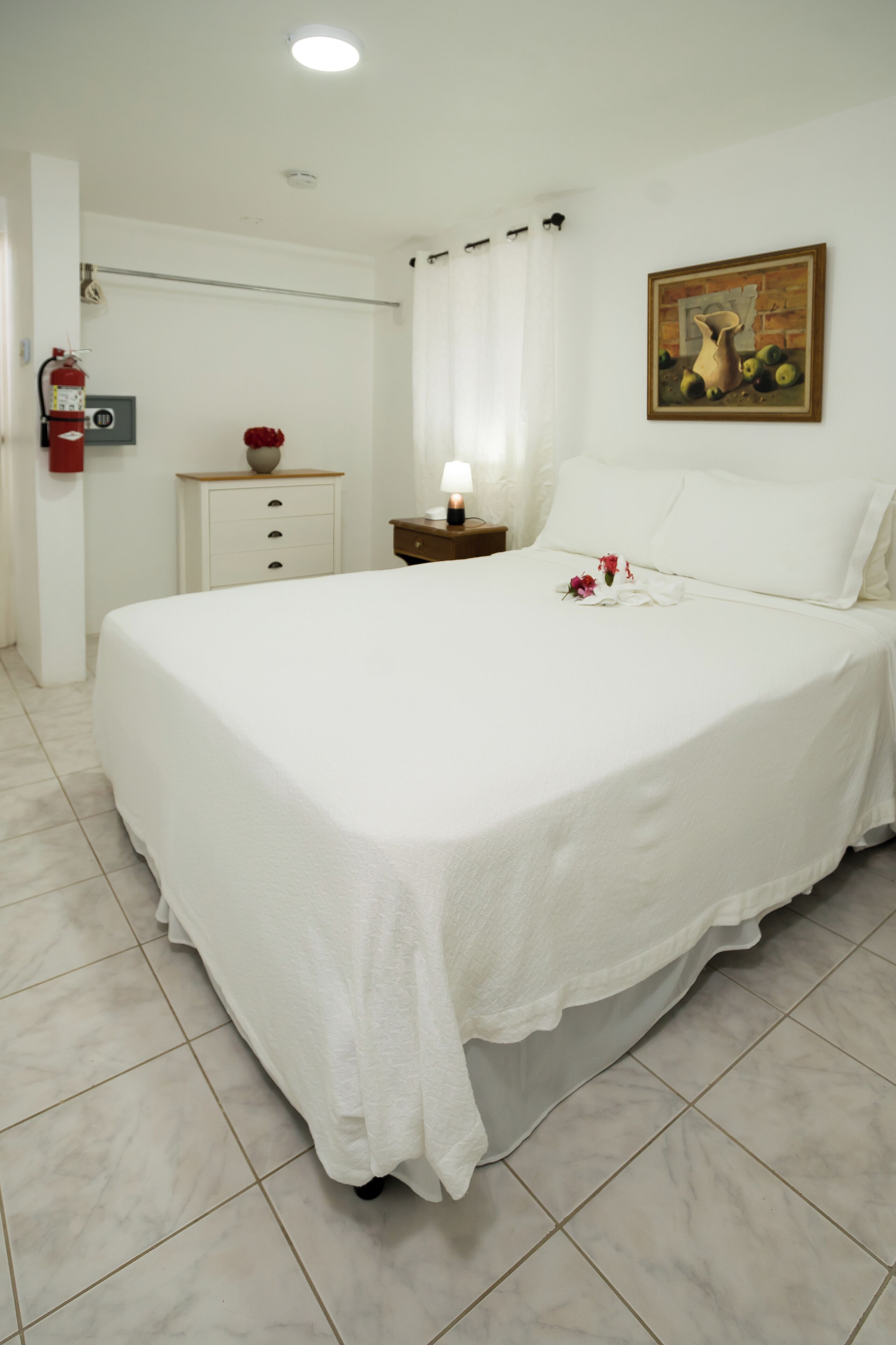 A neatly made bed with a white bedspread, a nightstand with a lamp, and a painting on the wall.